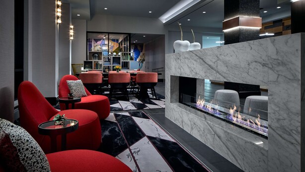 Een moderne lobby met een open haard, rode zitplaatsen en een marmeren vloer.