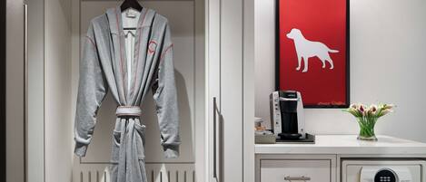A robe hanging in a closet, a framed dog silhouette, a coffee machine, and a vase with flowers on a counter.