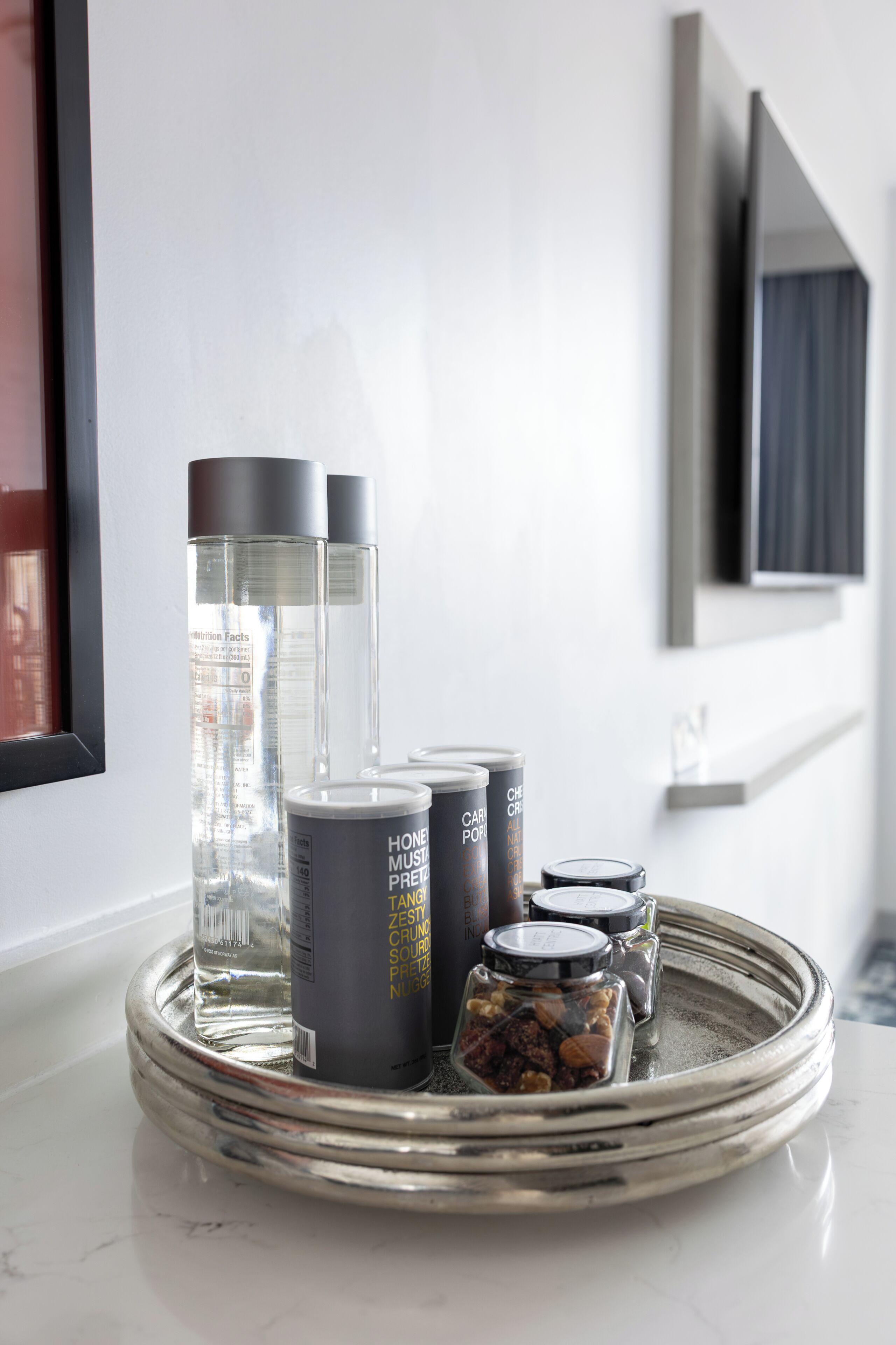 A tray with various containers on a marble countertop, including clear bottles and cans with labels, and a small jar with nuts.