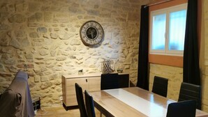 Un espace repas avec un mur en pierre, un plafond en bois et une grande table entourée de chaises.
