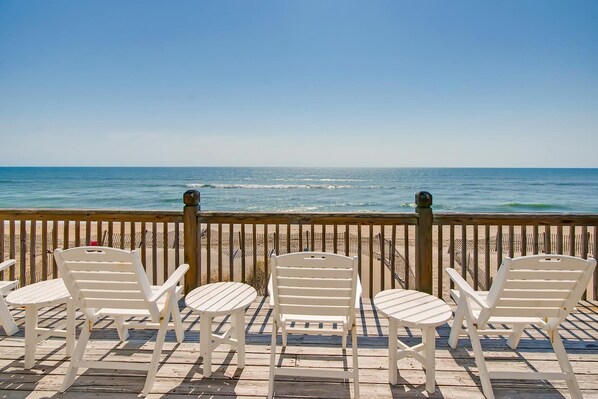 A wooden deck with white chairs and tables overlooking a beach with waves. - Premier Oceanfront w/ Private Pool, Hot Tub, Elevator, Sauna, Theater, Game Room (Avon)
