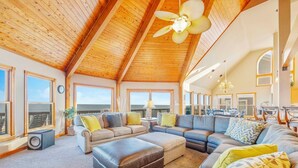 A spacious living area with a high ceiling, large windows, and a view of the ocean. - Premier Oceanfront w/ Private Pool, Hot Tub, Elevator, Sauna, Theater, Game Room (Avon)