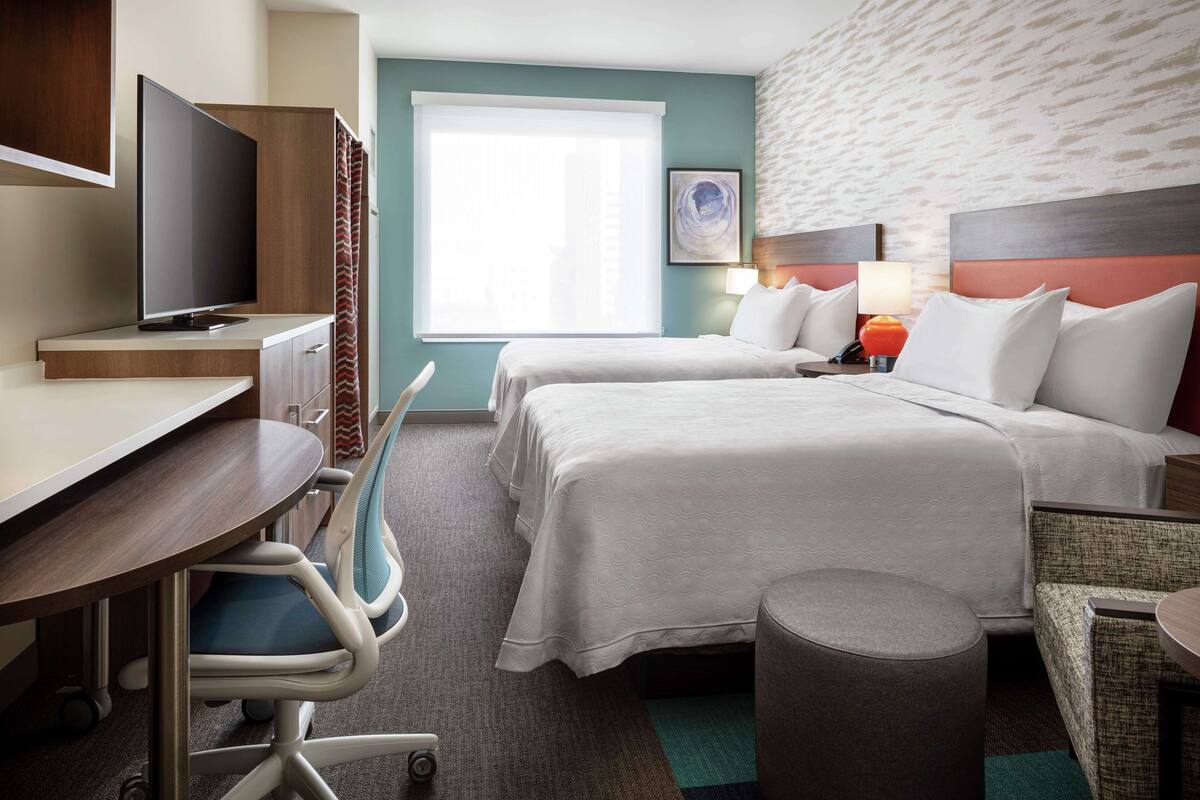 Una habitación de hotel con dos camas, un escritorio, un televisor y una silla.