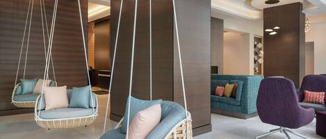 A modern lobby with hanging wicker chairs, a teal sofa, and a purple armchair.