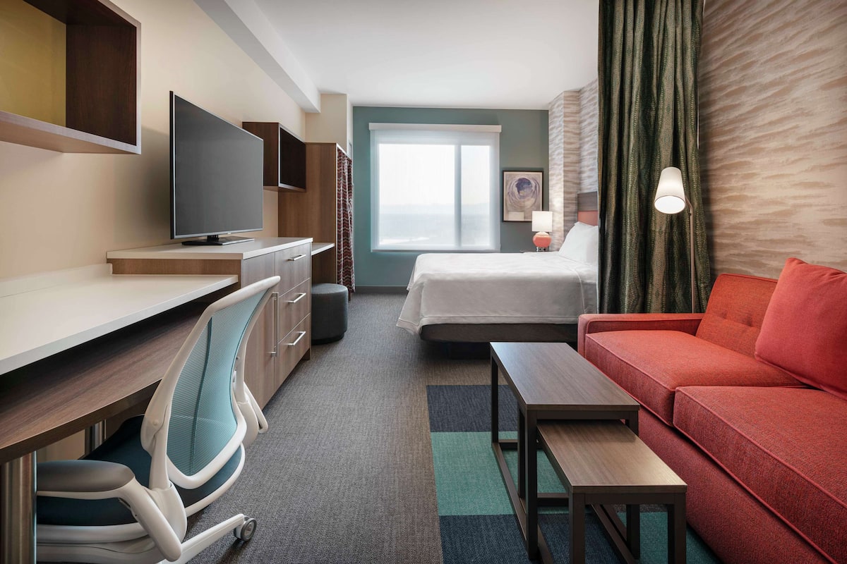 Habitación de hotel con cama, escritorio, silla, televisor, sofá y lámpara.
