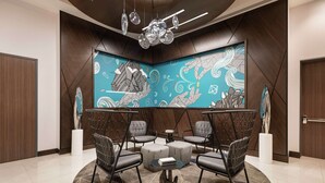 A modern lounge area with a geometric patterned wall, a central round table, and four grey upholstered chairs.