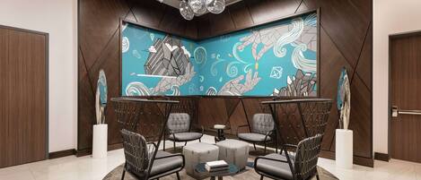 A modern lounge area with a geometric patterned wall, a central round table, and four grey upholstered chairs.