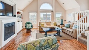 A spacious living room with a fireplace, a large TV, and a cozy seating area with a sofa and armchairs.