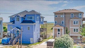 A residential area with a blue house featuring a prominent tower-like structure, a beige multi-story building, and a small attached garage.