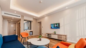 A modern living room with a sofa, chairs, a coffee table, a TV, and a kitchenette. - Holiday Inn Express Taizhou CMC by IHG (Taizhou)