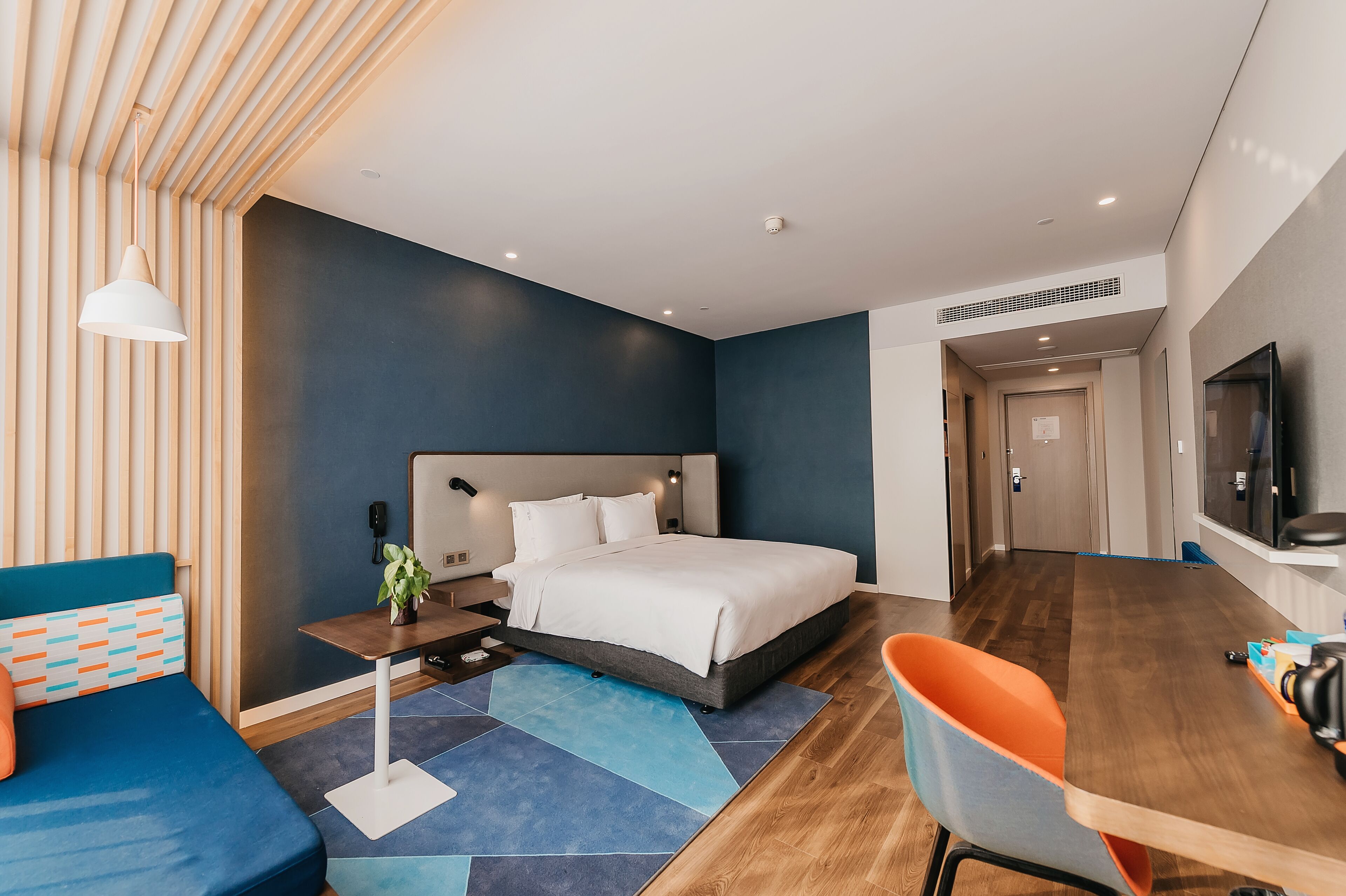 A modern hotel room with a large bed, a desk, and a TV.