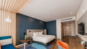 A modern hotel room with a large bed, a desk, and a TV.