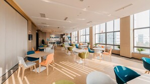 A spacious, well-lit dining area with multiple tables and chairs, large windows offering views of the city, and a kitchen area in the background. - Holiday Inn Express Taizhou CMC by IHG (Taizhou)
