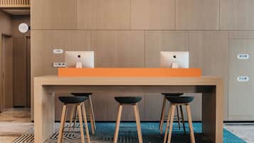 A modern hotel lobby with a wooden reception desk, two Apple iMac computers, and three black bar stools.