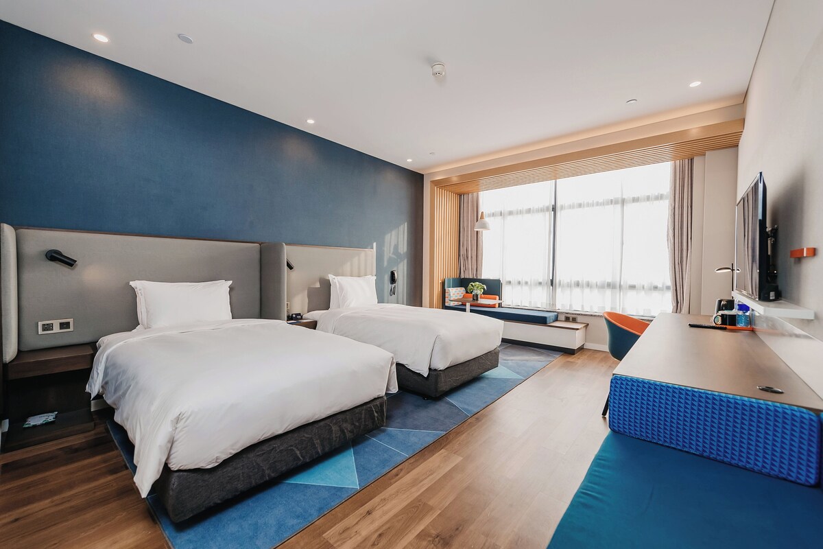 Une chambre d’hôtel moderne avec deux lits, un bureau et une grande fenêtre.