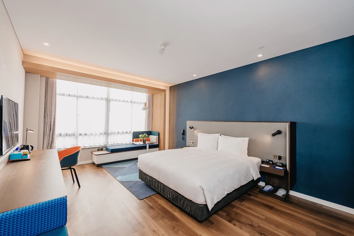 Una habitación de hotel moderna con una cama grande, un escritorio con silla, un televisor y una ventana con cortinas.