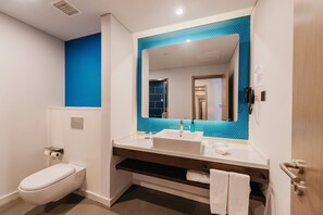 Une salle de bain moderne avec des toilettes blanches, un lavabo avec un pare-éclaboussures bleu et un miroir.