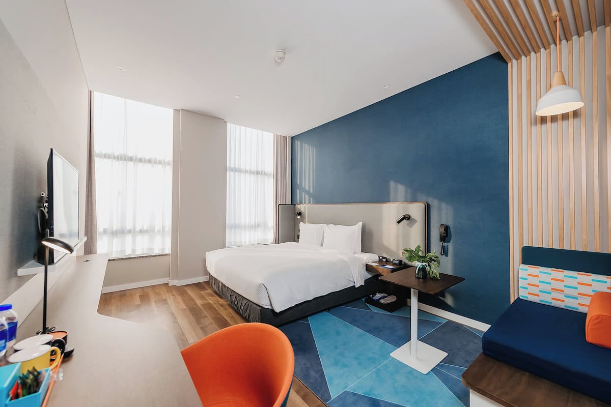 Una habitación de hotel moderna con una cama grande, un escritorio con una silla, un sofá y un televisor.
