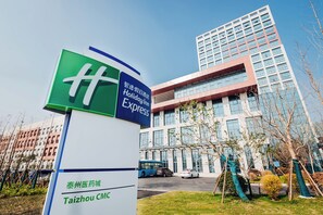 A Holiday Inn Express sign with a Taizhou CMG sign below it, in front of a modern building with multiple floors and large windows. - Holiday Inn Express Taizhou CMC by IHG (Taizhou)