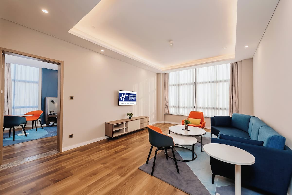 Una habitación de hotel moderna con suelo de madera, un sofá azul, una mesa de centro redonda y un televisor montado en la pared.