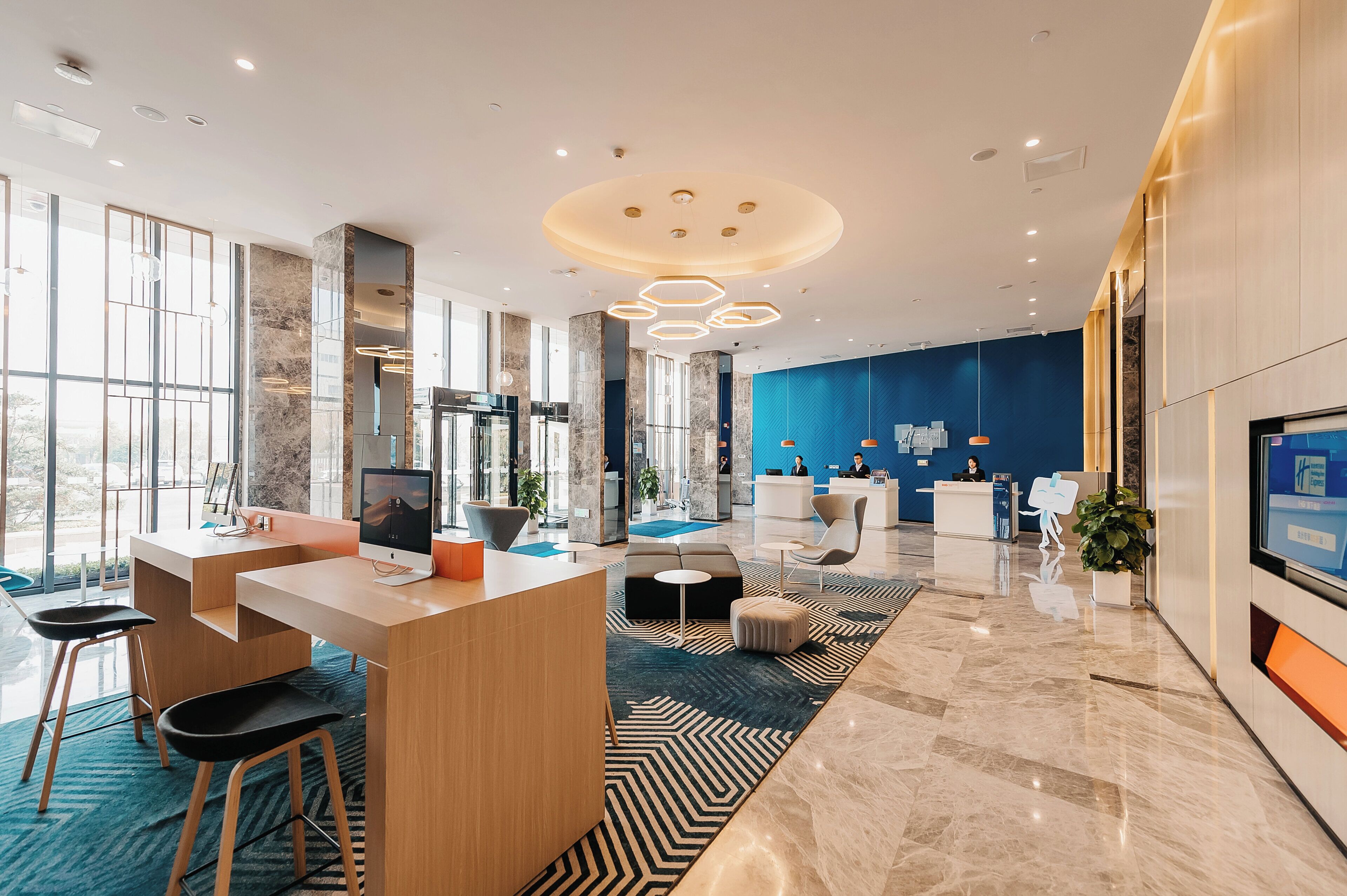 A modern hotel lobby with a reception desk, seating area, and large windows.