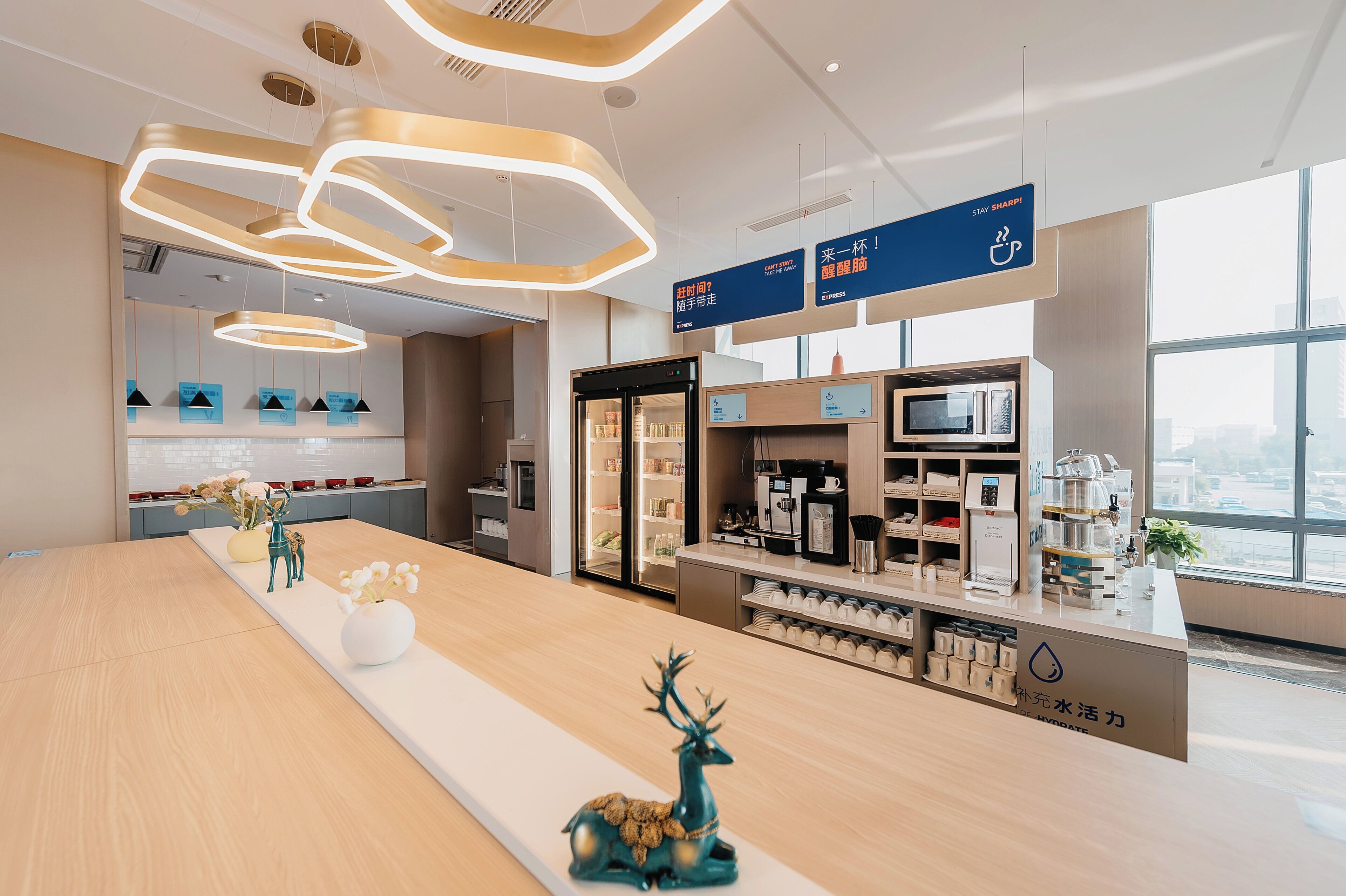 Un moderno vestíbulo de hotel con un mostrador de recepción alargado, una cafetería y vistas a la ciudad a través de amplios ventanales.