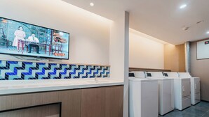 Une buanderie moderne équipée d’un téléviseur à écran plat fixé au mur, d’un pare-feu décoratif et d’une rangée de machines à laver superposées.