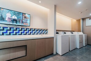 Une buanderie moderne équipée d’un téléviseur à écran plat fixé au mur, d’un pare-feu décoratif et d’une rangée de machines à laver superposées.