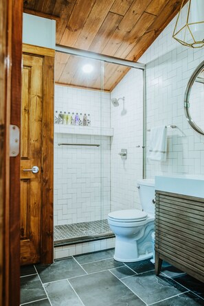 A bathroom with a wooden door, white tiled walls, a white toilet, and a shower area. - Enjoy the peace & quiet of beautiful Nashville, Indiana. (Nashville)