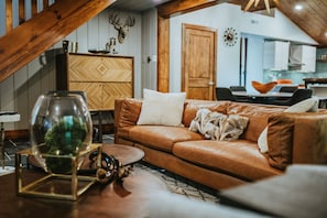 A cozy living room with a brown leather sofa, a glass coffee table, and a wooden cabinet.