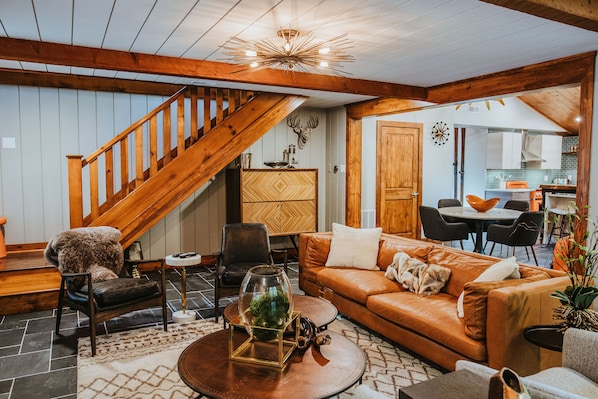 A spacious living room with a wooden staircase, a leather sofa, a coffee table, and a dining area in the background.