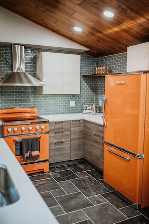 A kitchen with a vintage orange stove, a matching refrigerator, and wooden cabinets.