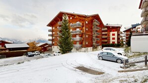 A multi-story wooden building with balconies, surrounded by snow-covered ground and parked cars. - Pracondu 1 206 - OUTDOOR & FUN  apartment 4 pers (Haute-Nendaz)