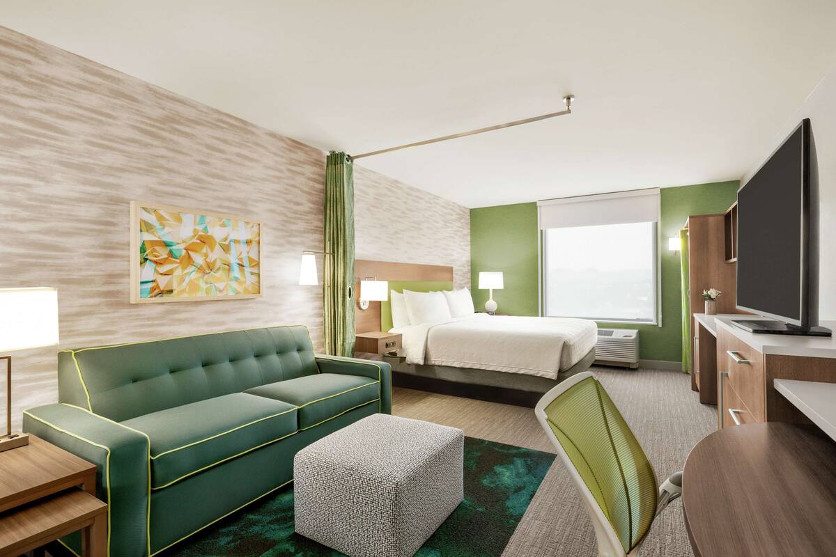 Een hotelkamer met een groene bank, een bed, een bureau en een televisie.