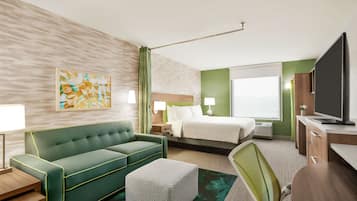 A hotel room with a green sofa, a bed, a desk, and a television.