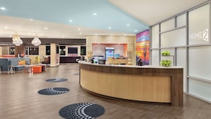 A modern hotel lobby with a curved reception desk, seating area with sofas and chairs, and a large wall with a 'HOME2' sign. - Home2 Suites by Hilton Scottsdale Salt River (Scottsdale)