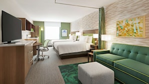 A hotel room with a bed, a green sofa, a TV, a desk, and a green carpet. - Home2 Suites by Hilton Scottsdale Salt River (Scottsdale)