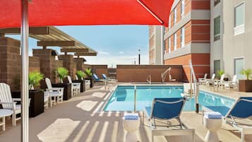 Una piscina al aire libre, sombrillas, sillones reclinables de piscina