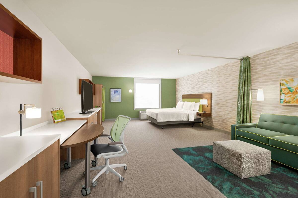 Een hotelkamer met een bureau, stoel, bed en een groene bank.