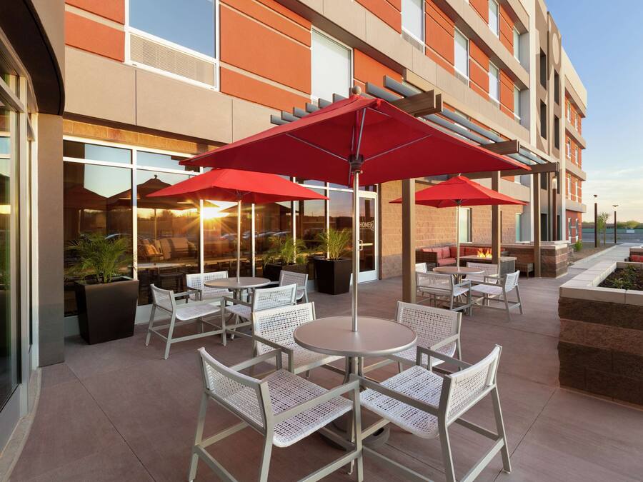 Un espace extérieur aménagé en terrasse, avec des tables rondes et des chaises en osier blanc, des parasols rouges et des plantes en pot.