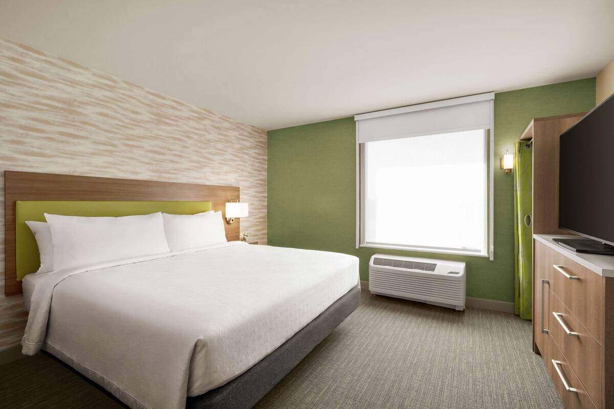 Een hotelkamer met een bed, een televisie, een raam met gordijnen en een wandradiator.