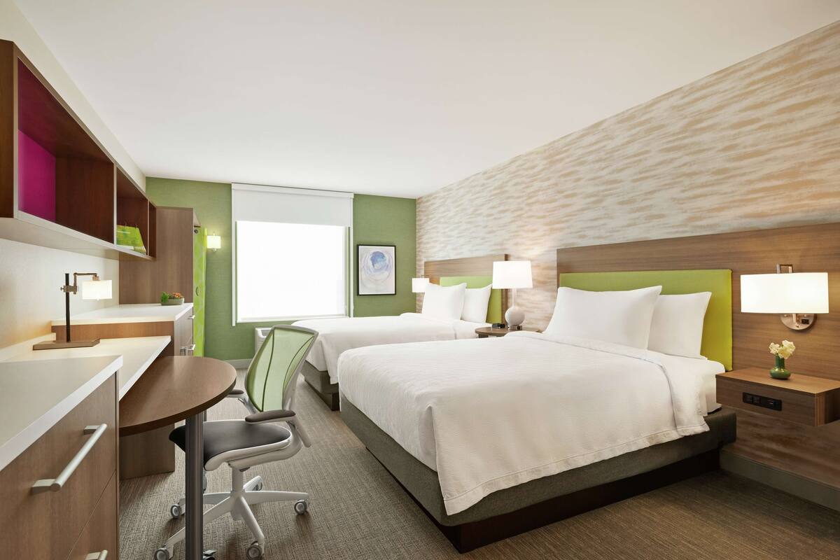 Een hotelkamer met twee bedden, een bureau, een stoel en een klein tafeltje.