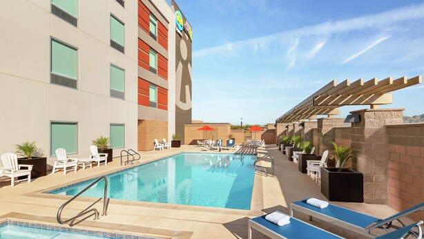 A hotel pool area with sun loungers, a children's play area, and a building with a sign. - Home2 Suites by Hilton Scottsdale Salt River (Scottsdale)