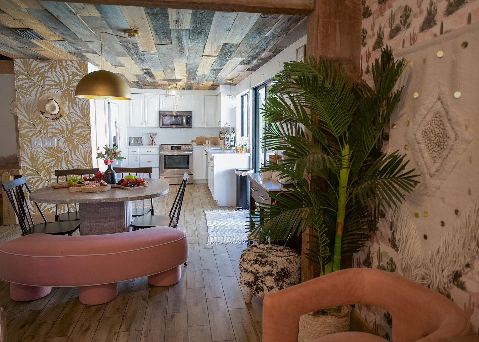 A modern kitchen with white cabinets, a central island, and a dining area with a pink ottoman and chairs.