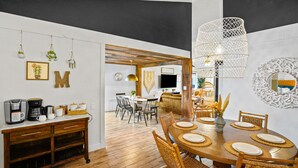 A dining area with a wooden table set for four, surrounded by wicker chairs, and a modern pendant light fixture above.