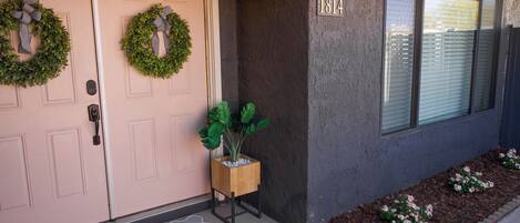 A house with a double door, a welcome mat, a number plaque, a potted plant, and a window with blinds.