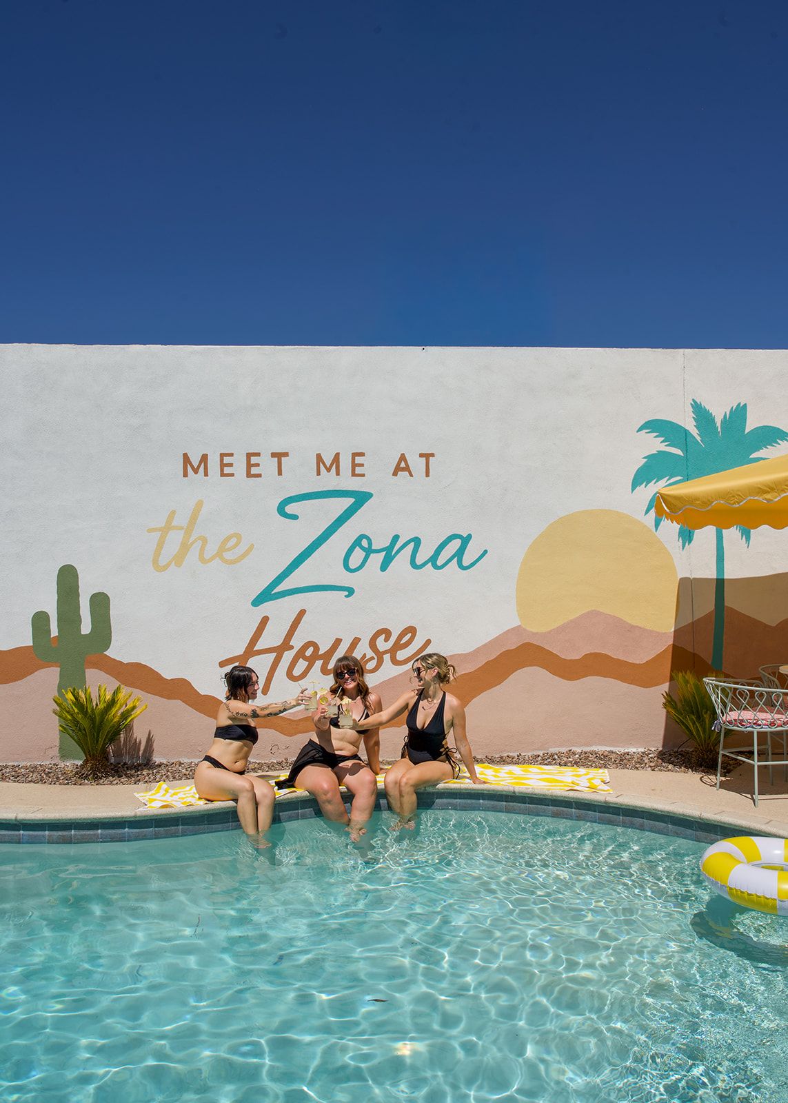 A pool area with a mural that reads 'MEET ME AT the Zona House' and includes desert-themed artwork.
