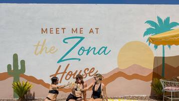 A pool area with a mural that reads 'MEET ME AT the Zona House' and includes desert-themed artwork.