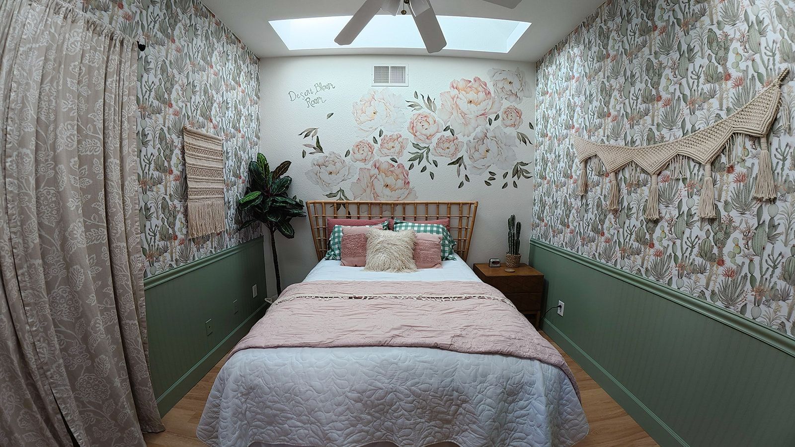 Une chambre avec une lucarne, un papier peint à motifs floraux, un lit recouvert d’une courtepointe à carreaux et une table de chevet sur laquelle se trouve un cactus.
