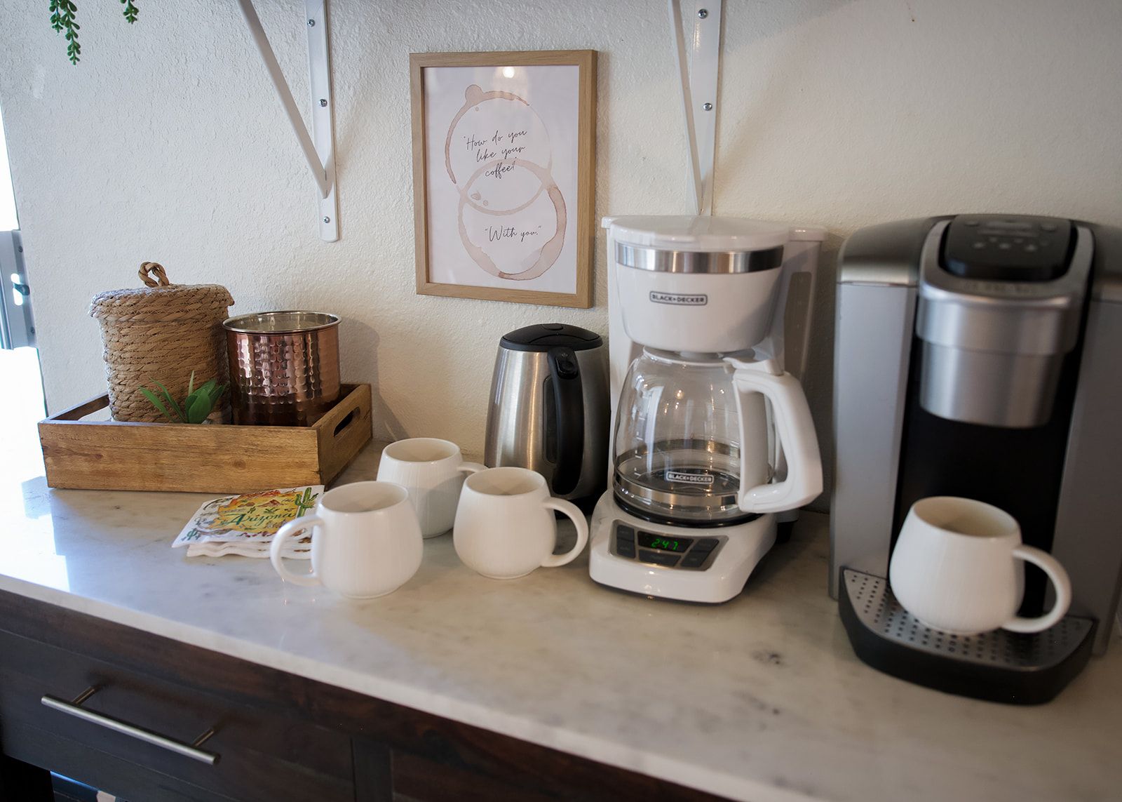 Una encimera de cocina con una cafetera, un hervidor y varias tazas.